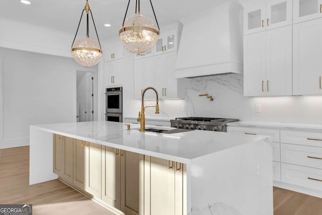 kitchen featuring premium range hood, decorative light fixtures, a center island with sink, stainless steel appliances, and backsplash