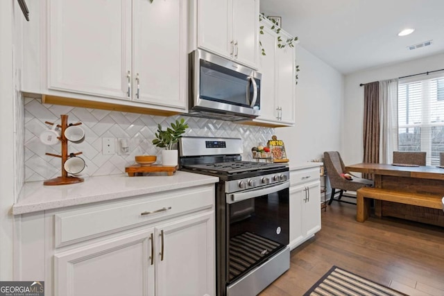 kitchen featuring light hardwood / wood-style flooring, appliances with stainless steel finishes, backsplash, light stone countertops, and white cabinets