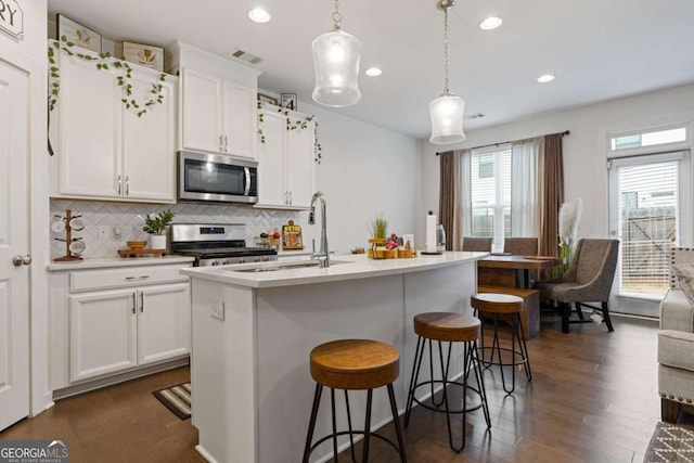 kitchen featuring pendant lighting, appliances with stainless steel finishes, white cabinetry, a center island with sink, and decorative backsplash