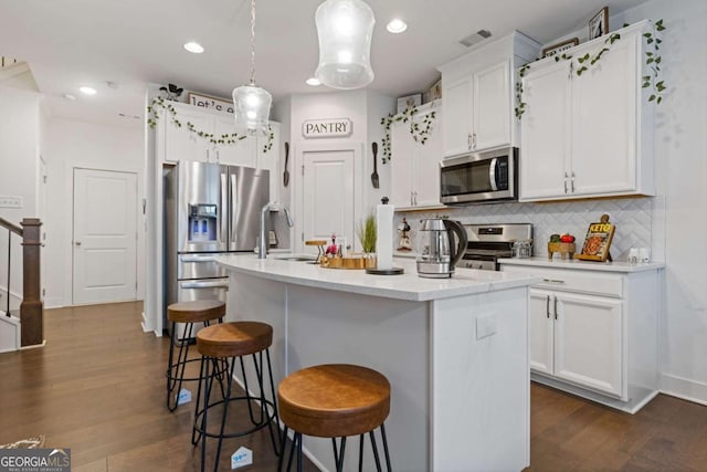 kitchen featuring appliances with stainless steel finishes, decorative light fixtures, tasteful backsplash, sink, and a center island with sink