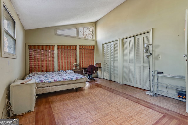 bedroom with light parquet floors, high vaulted ceiling, two closets, and a textured ceiling