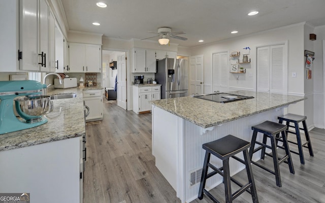 kitchen with stainless steel refrigerator with ice dispenser, light stone counters, ornamental molding, white cabinets, and a kitchen island