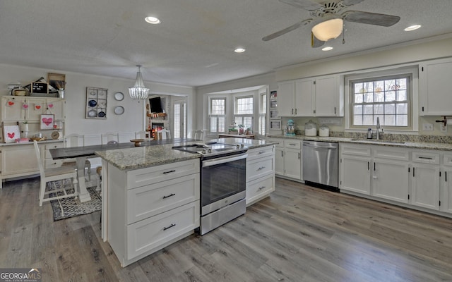 kitchen featuring appliances with stainless steel finishes, decorative light fixtures, white cabinetry, sink, and a center island