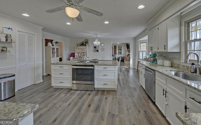 kitchen featuring sink, appliances with stainless steel finishes, white cabinetry, hanging light fixtures, and light stone counters