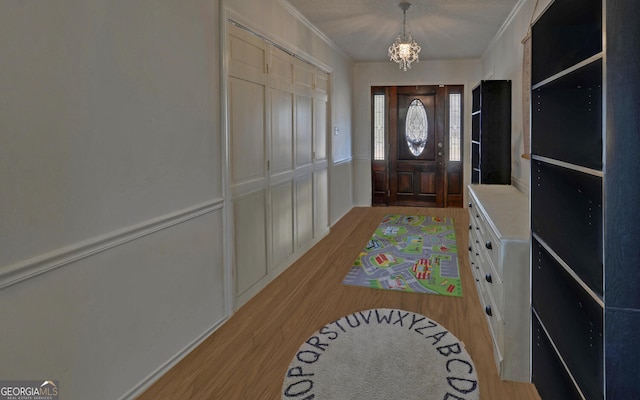 entryway with crown molding, a chandelier, light hardwood / wood-style floors, and a textured ceiling