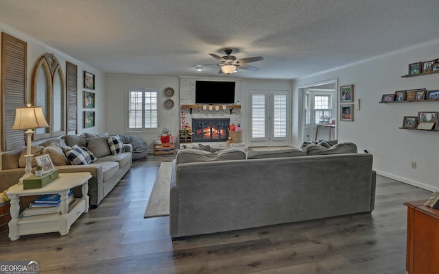 living room featuring dark wood-type flooring, a textured ceiling, ornamental molding, ceiling fan, and a fireplace