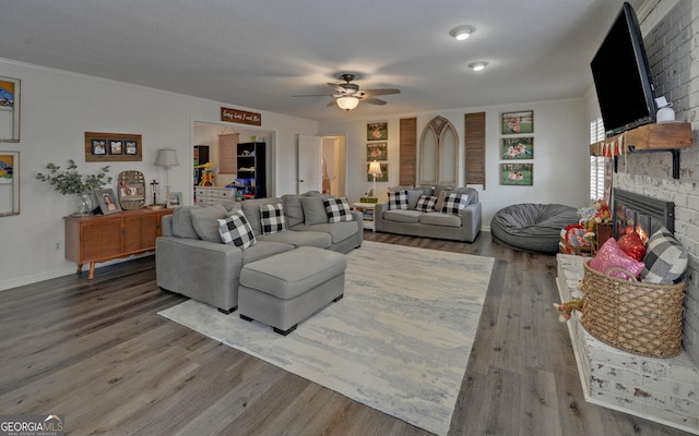 living room with a fireplace, wood-type flooring, ornamental molding, ceiling fan, and a textured ceiling