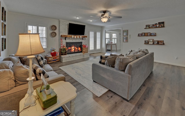 living room featuring ceiling fan, wood-type flooring, a fireplace, and a textured ceiling