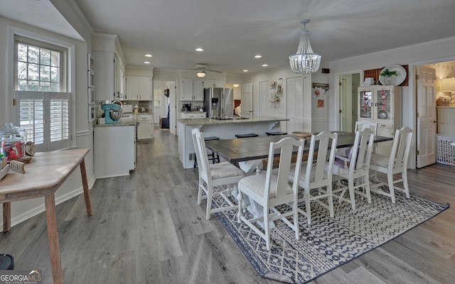 dining area with ceiling fan with notable chandelier and light hardwood / wood-style flooring