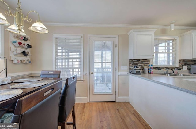 kitchen with white cabinetry, decorative backsplash, hanging light fixtures, crown molding, and light hardwood / wood-style flooring