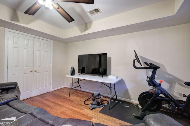 workout room with ceiling fan, wood-type flooring, and a tray ceiling