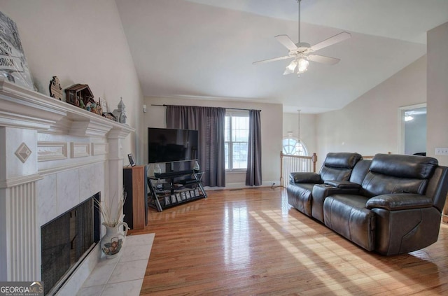 living room featuring a tiled fireplace, lofted ceiling, ceiling fan, and light wood-type flooring