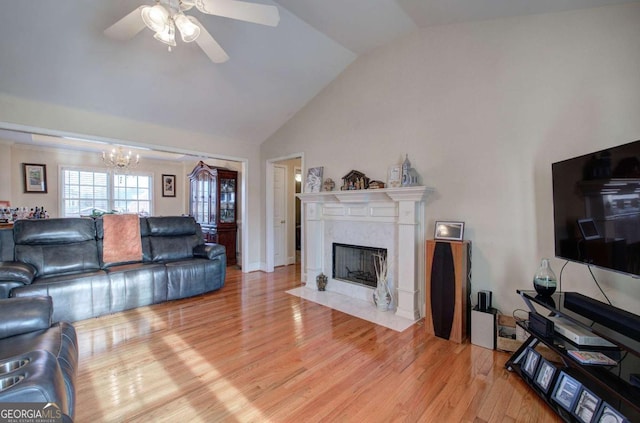 living room with ceiling fan with notable chandelier, lofted ceiling, a high end fireplace, and light hardwood / wood-style floors