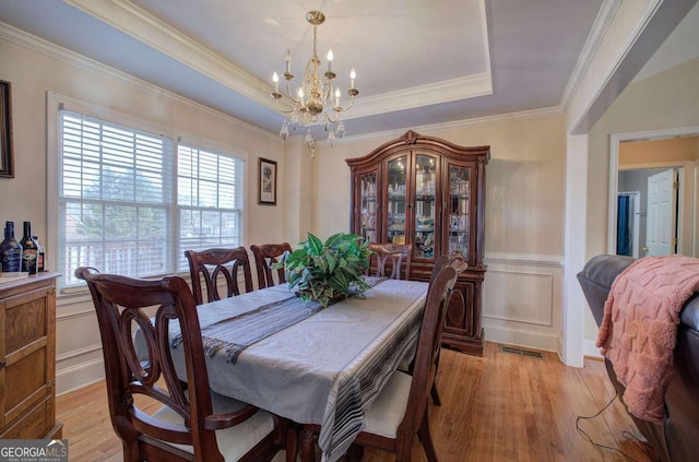 dining room with a raised ceiling, a healthy amount of sunlight, a chandelier, and light hardwood / wood-style floors