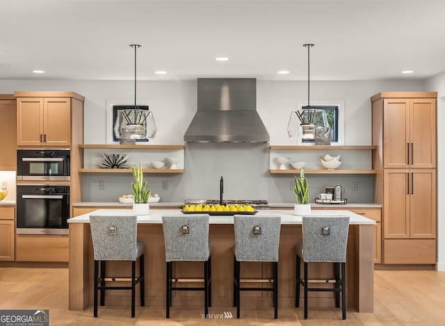 kitchen featuring wall chimney exhaust hood, decorative light fixtures, and a center island with sink