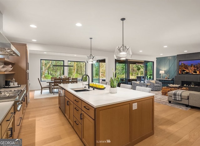 kitchen with a kitchen island with sink, sink, hanging light fixtures, and light wood-type flooring