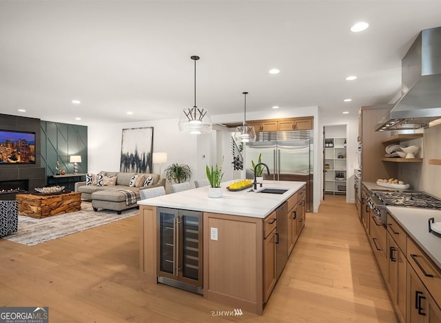 kitchen with wine cooler, sink, decorative light fixtures, island exhaust hood, and a kitchen island with sink