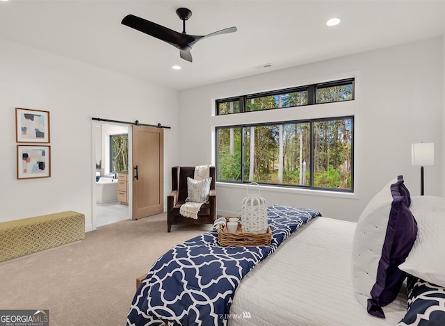 carpeted bedroom with a barn door, ceiling fan, and ensuite bath