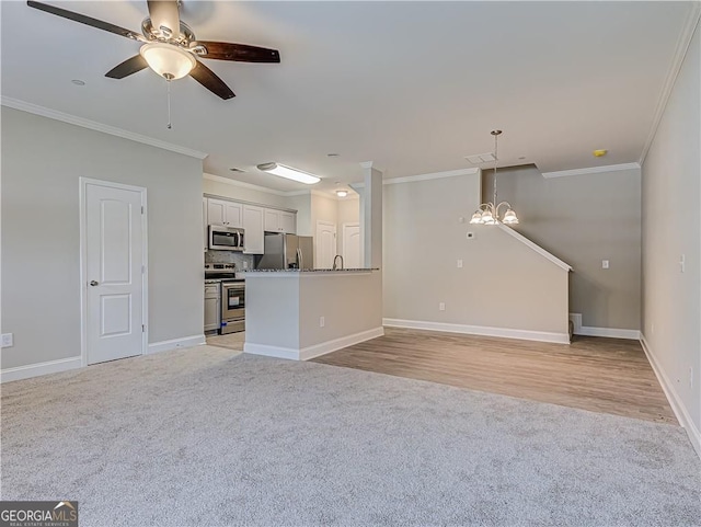 unfurnished living room with light carpet, ceiling fan with notable chandelier, baseboards, and crown molding