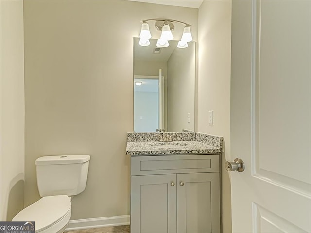 half bath featuring visible vents, vanity, toilet, and baseboards