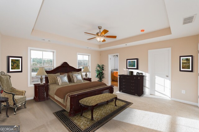 bedroom with light carpet, a raised ceiling, ceiling fan, and ensuite bathroom