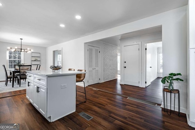 kitchen with a breakfast bar area, decorative light fixtures, a center island, dark hardwood / wood-style flooring, and white cabinets