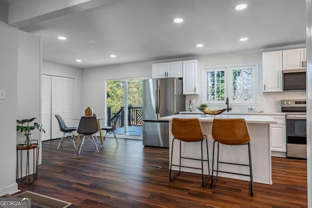 kitchen featuring dark wood-type flooring, stainless steel appliances, tasteful backsplash, white cabinets, and a kitchen island