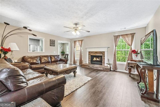 living room featuring dark wood-type flooring, ceiling fan, a fireplace, and a textured ceiling