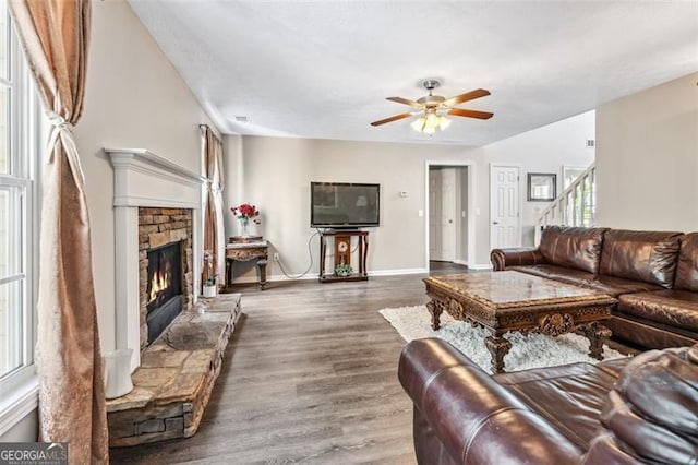 living room featuring a stone fireplace, dark hardwood / wood-style floors, and ceiling fan