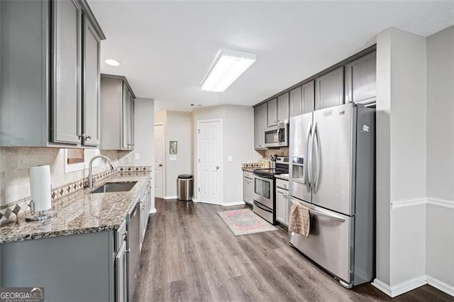 kitchen with gray cabinets, appliances with stainless steel finishes, sink, hardwood / wood-style flooring, and light stone countertops