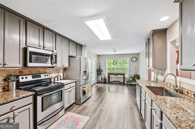 kitchen featuring sink, decorative light fixtures, light hardwood / wood-style flooring, stainless steel appliances, and decorative backsplash