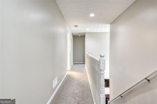 hall featuring light colored carpet and a textured ceiling