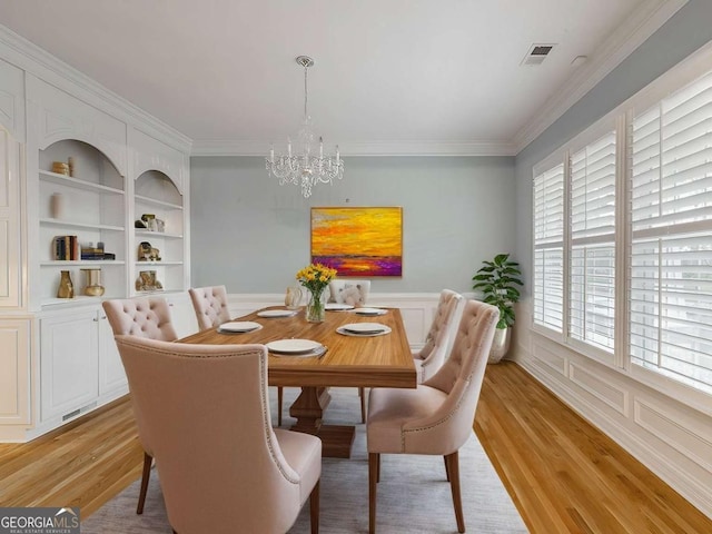 dining area with a wealth of natural light, a notable chandelier, light hardwood / wood-style floors, crown molding, and built in shelves