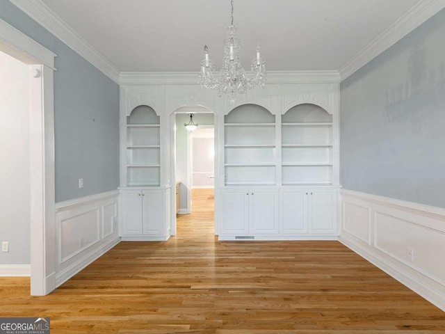 unfurnished dining area featuring ornamental molding, built in features, an inviting chandelier, and light hardwood / wood-style floors