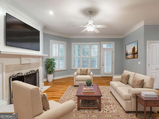 living room featuring crown molding, a fireplace, ceiling fan, and light wood-type flooring