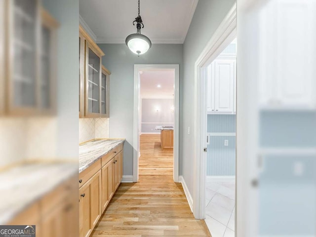 kitchen with backsplash, ornamental molding, light stone countertops, light brown cabinets, and light wood-type flooring