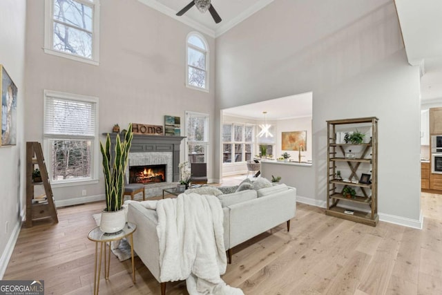 living room with a stone fireplace, crown molding, light wood-type flooring, ceiling fan, and a high ceiling