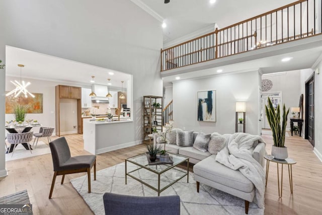 living room with crown molding, a towering ceiling, a chandelier, and light wood-type flooring