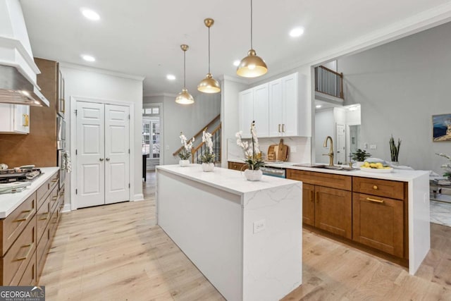 kitchen with sink, white cabinetry, hanging light fixtures, a kitchen island, and custom range hood