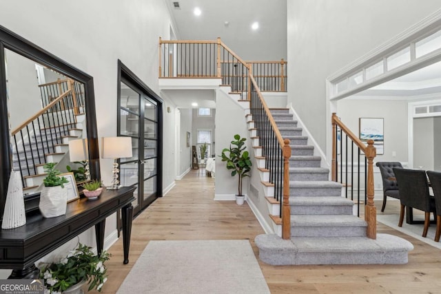 entryway with a high ceiling, ornamental molding, and light hardwood / wood-style flooring