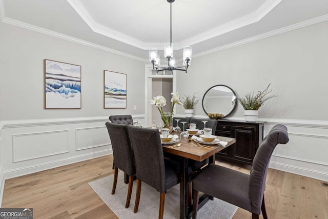 dining space with a notable chandelier, ornamental molding, a raised ceiling, and light wood-type flooring