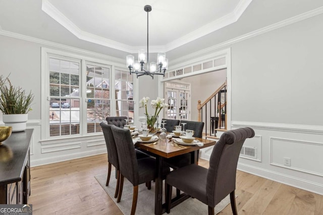 dining room with a raised ceiling, crown molding, an inviting chandelier, and light hardwood / wood-style floors