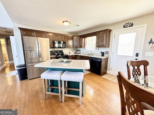 kitchen with sink, a kitchen island, black appliances, and light wood-type flooring