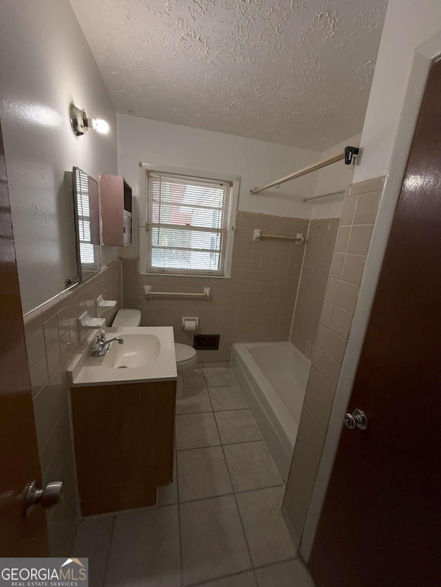 bathroom with tile walls, vanity, toilet, tile patterned floors, and a textured ceiling