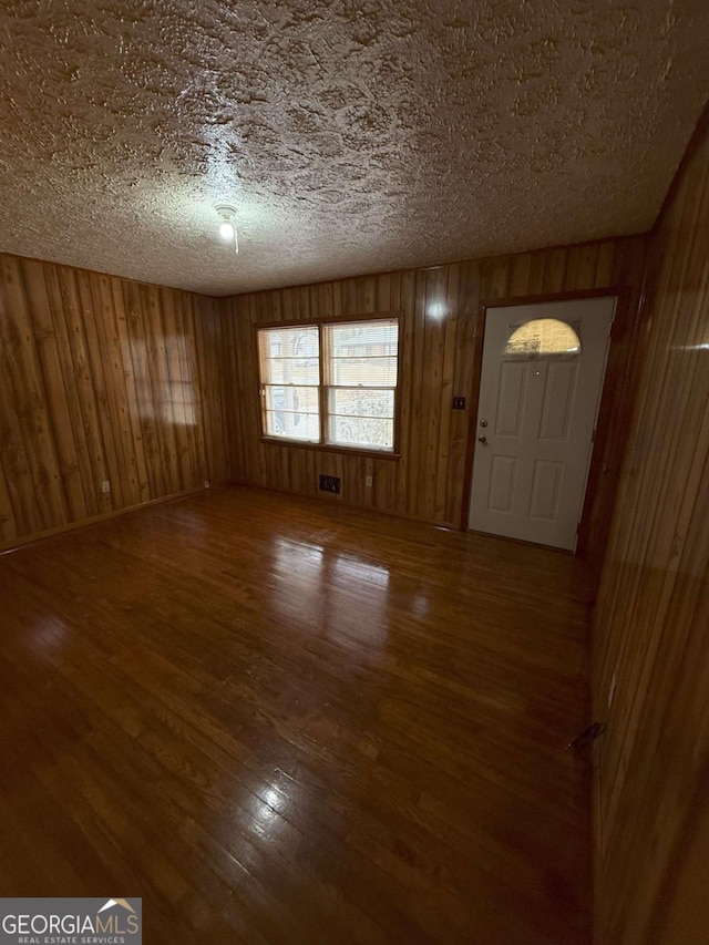 foyer entrance featuring hardwood / wood-style flooring, wooden walls, and a textured ceiling