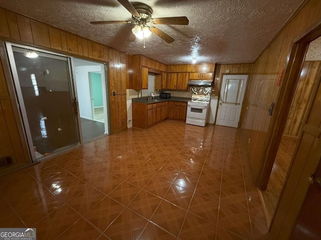 kitchen with wooden walls, white electric range oven, sink, and a textured ceiling