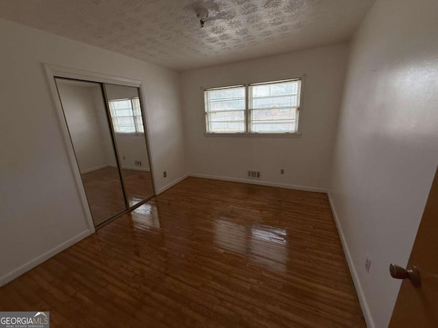 unfurnished bedroom with multiple windows, hardwood / wood-style floors, and a textured ceiling