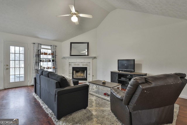 living room featuring vaulted ceiling, a fireplace, dark hardwood / wood-style flooring, ceiling fan, and a textured ceiling