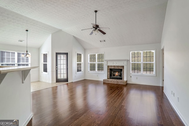 unfurnished living room with dark hardwood / wood-style flooring, vaulted ceiling, a brick fireplace, and a textured ceiling