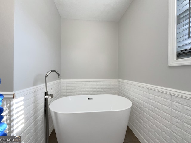 bathroom featuring a textured ceiling, tile walls, and a washtub